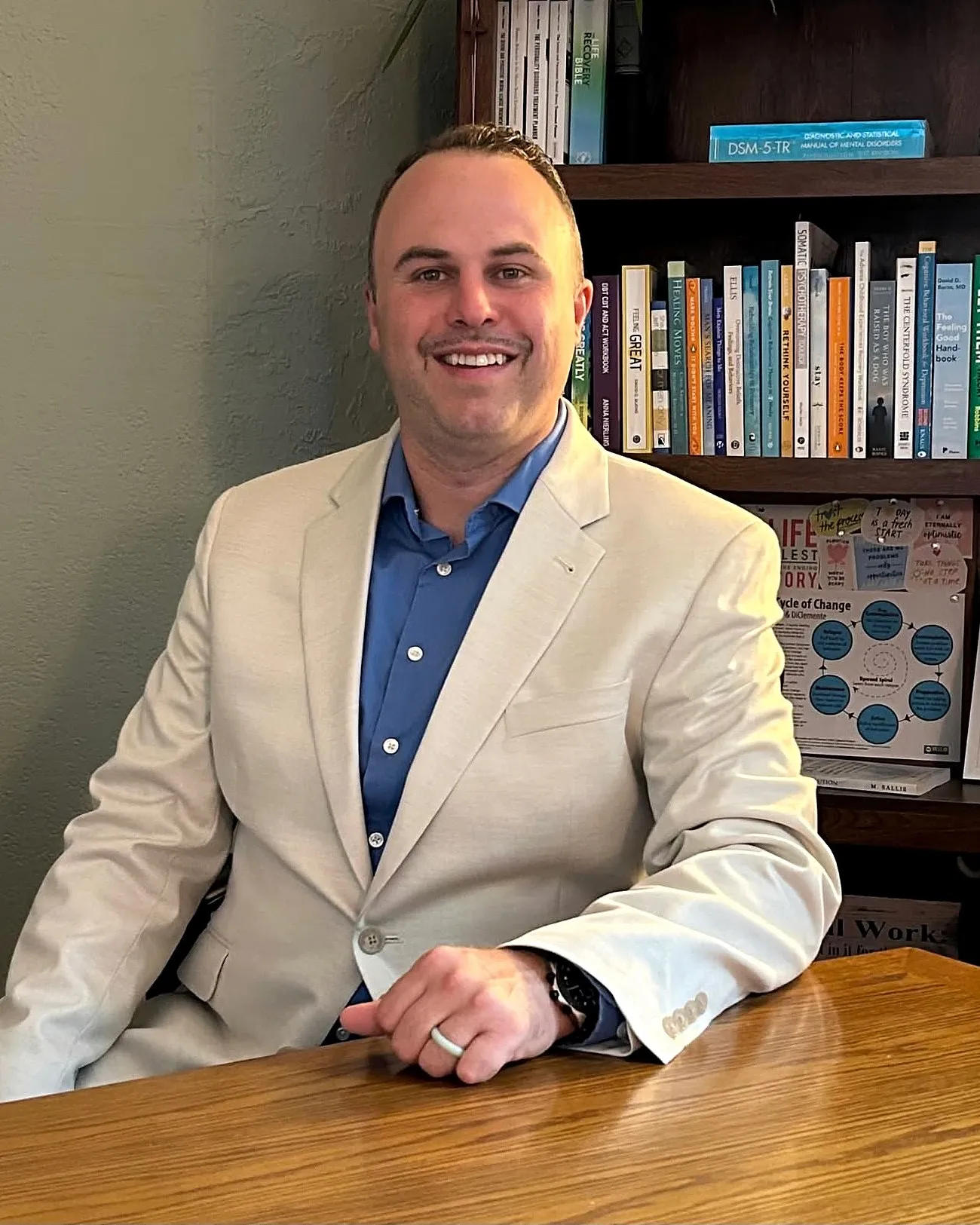 Ryan Rusnak smiling at his desk in front of a bookshelf in his office